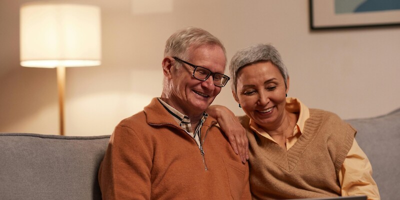 Man and Woman Sitting on Sofa While Looking at a Laptop